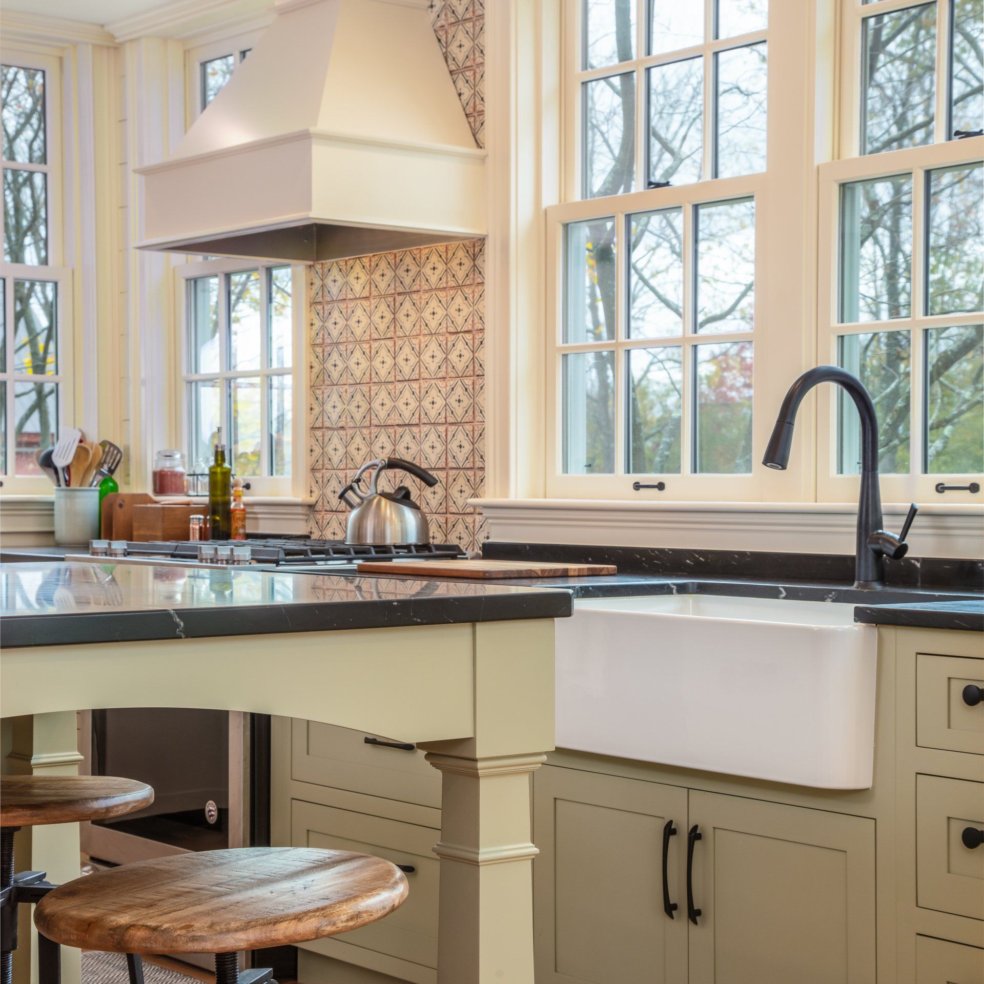 Bright kitchen with white cabinets, large windows, black countertops, and a farmhouse sink.