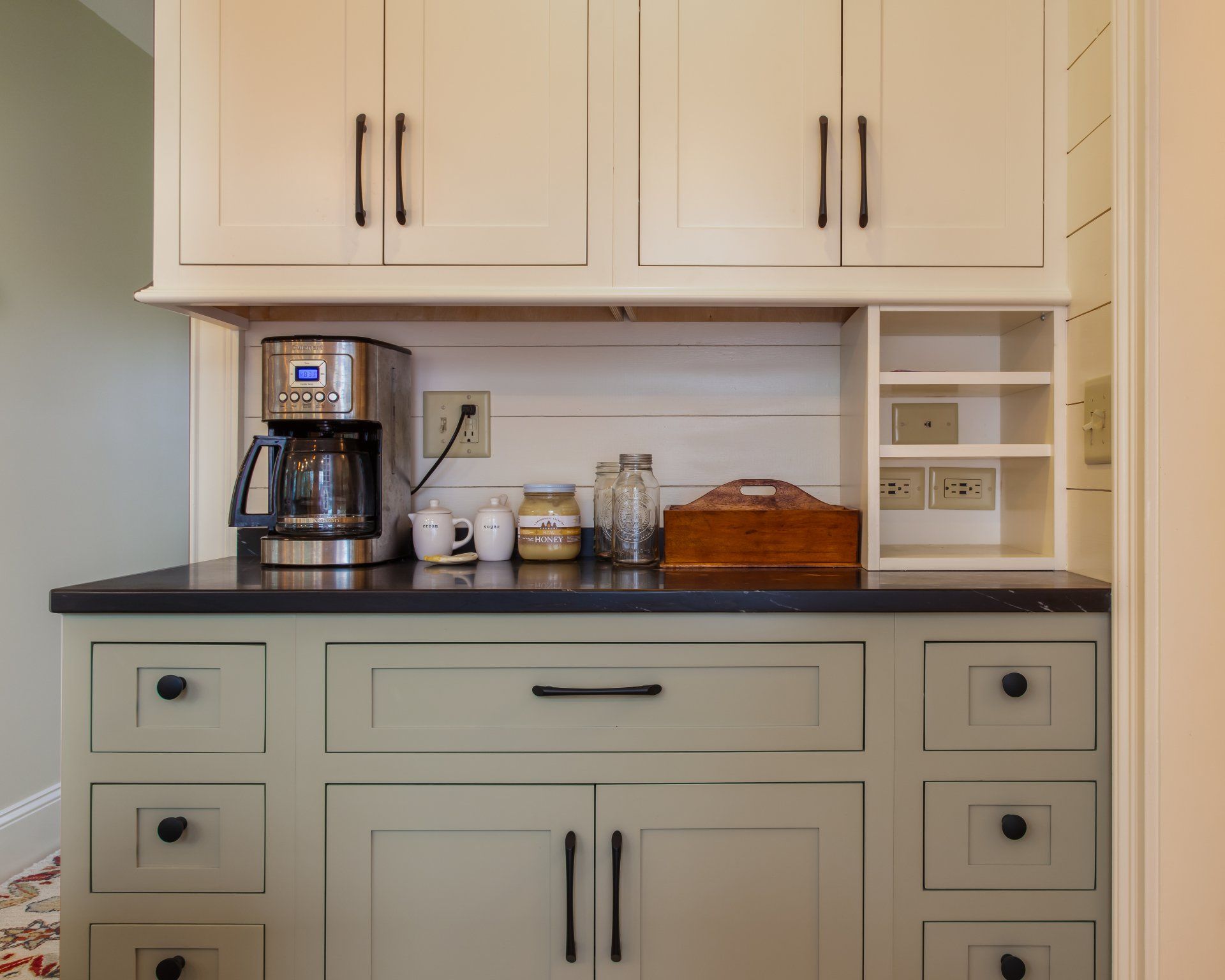 Built-in kitchen coffee station with cream cabinets, coffee maker, mugs, and countertop storage