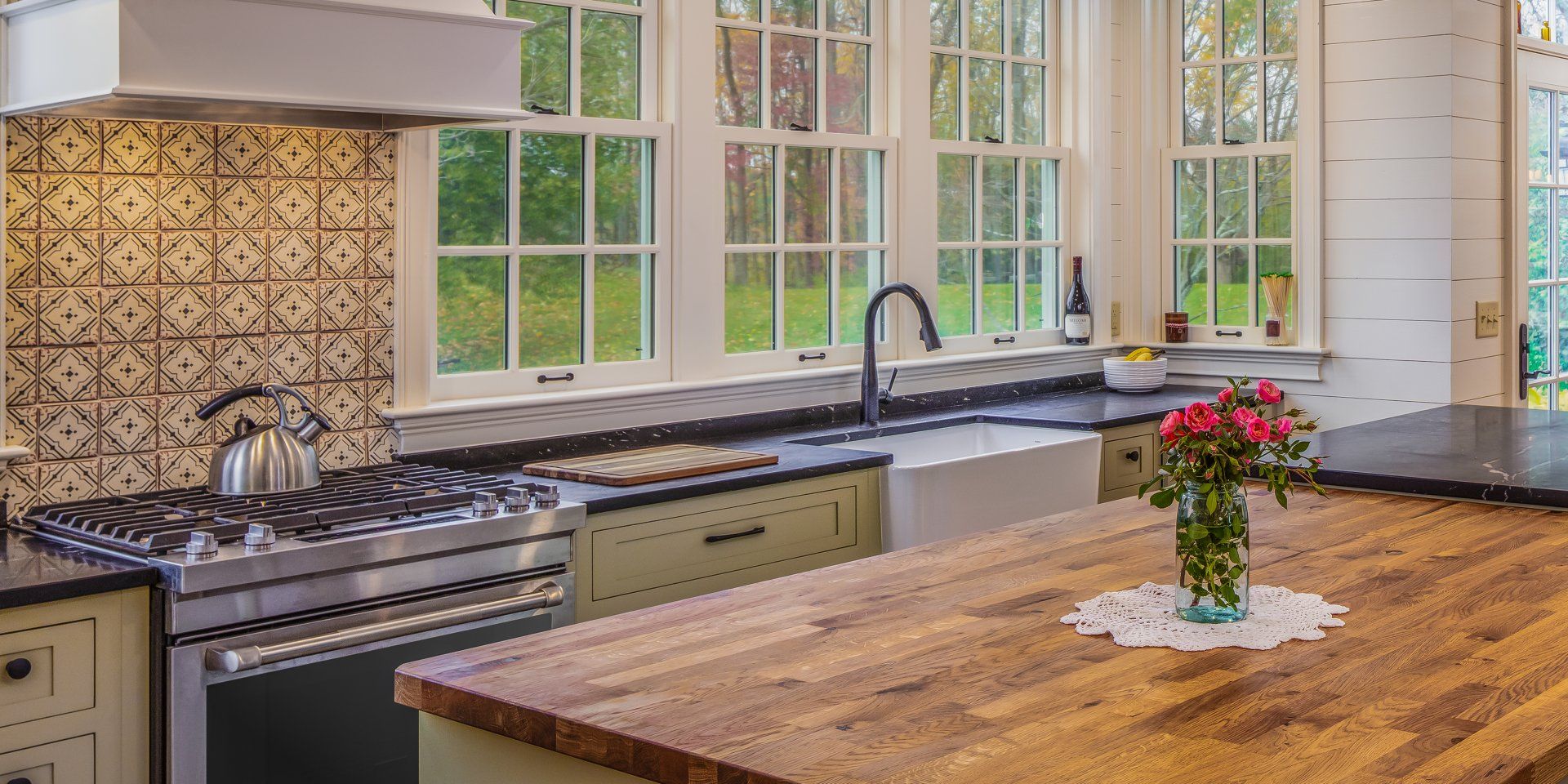 Bright kitchen with a gas stove, farmhouse sink, large windows, and a wooden island with flowers