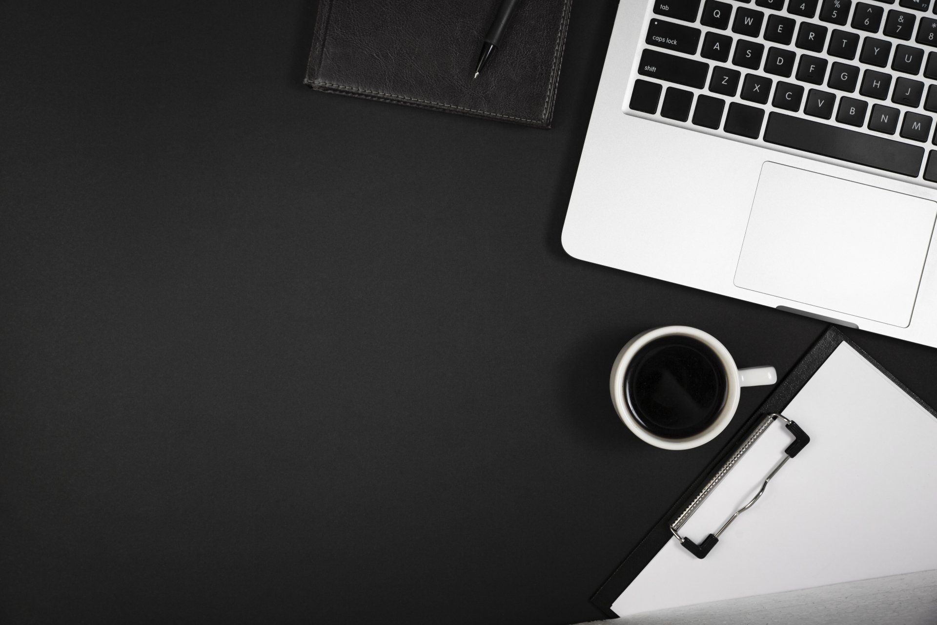Una foto in bianco e nero di una scrivania con un computer portatile, una tazza di caffè, un blocco per appunti e una penna.