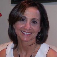 A smiling woman with shoulder-length dark hair wearing a sleeveless white top and a black beaded necklace.