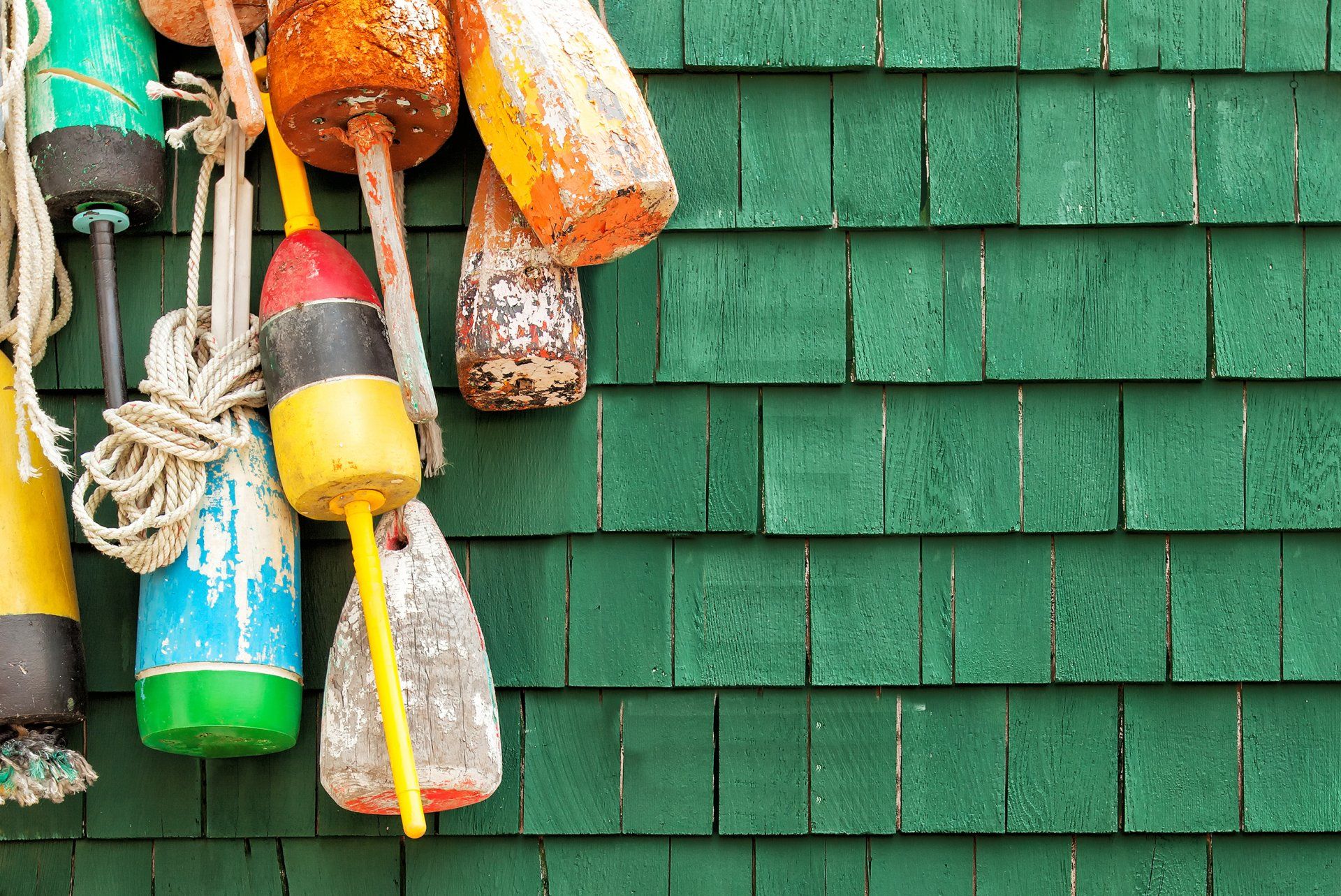 A collection of weathered, colorful fishing buoys hanging against a green shingled wall.