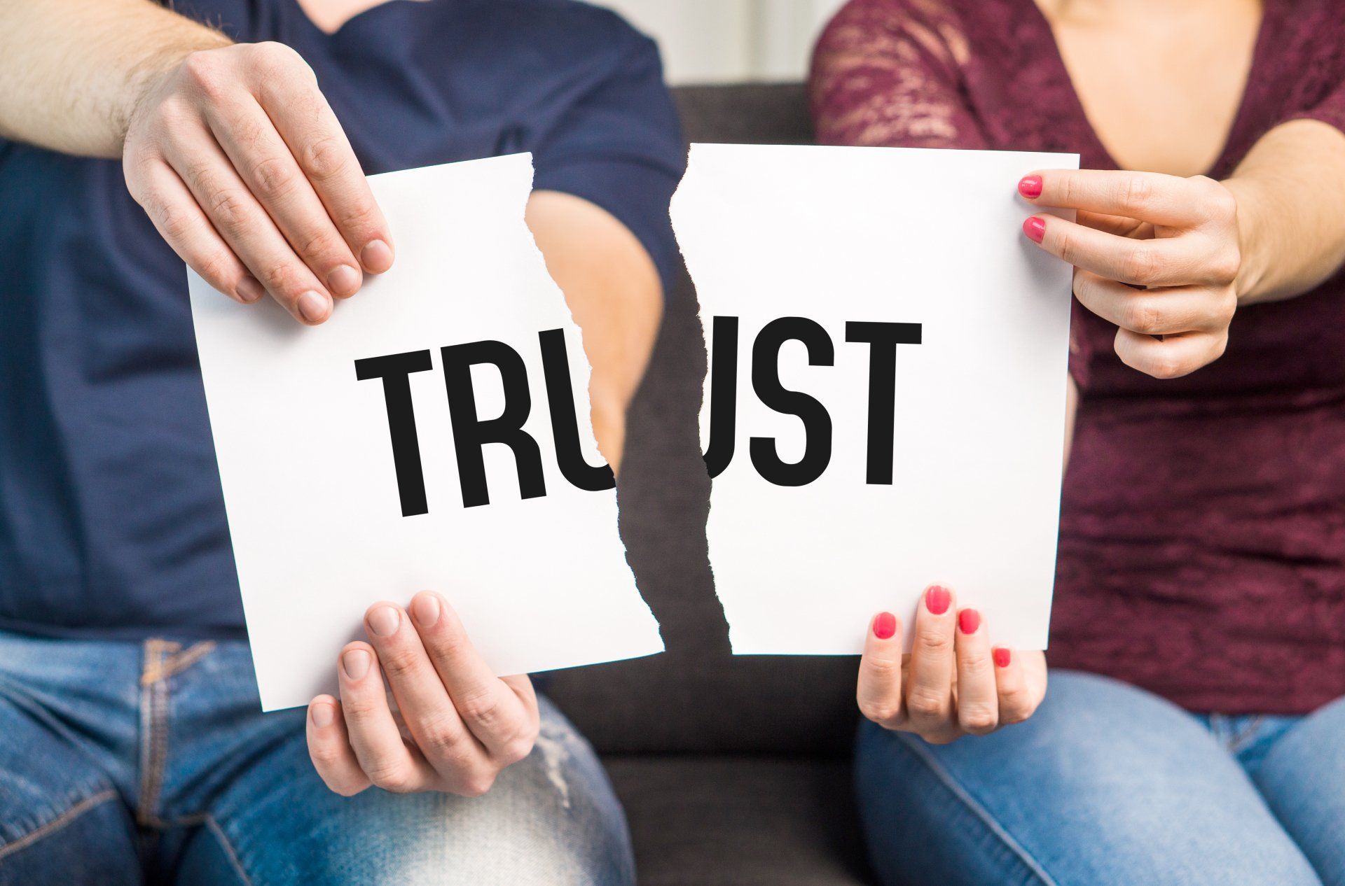 A man and woman sit together holding pieces of a torn sign that spells 