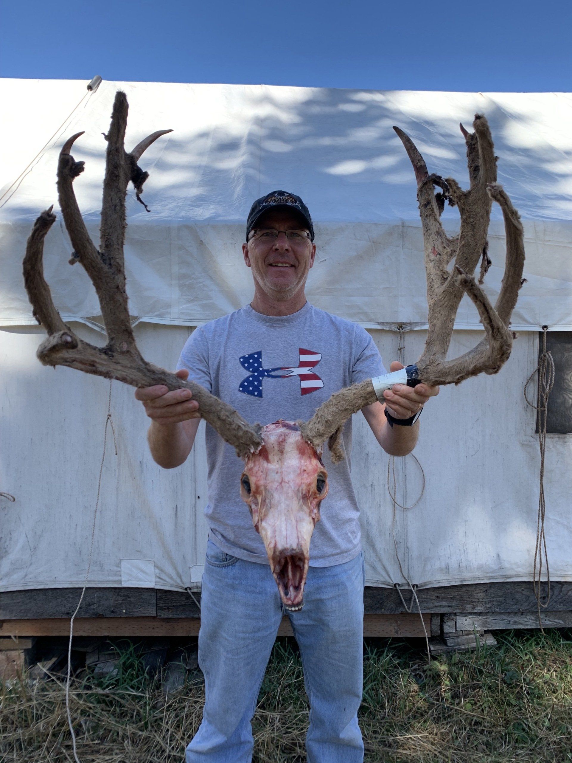 A man in an american flag shirt holds a deer skull