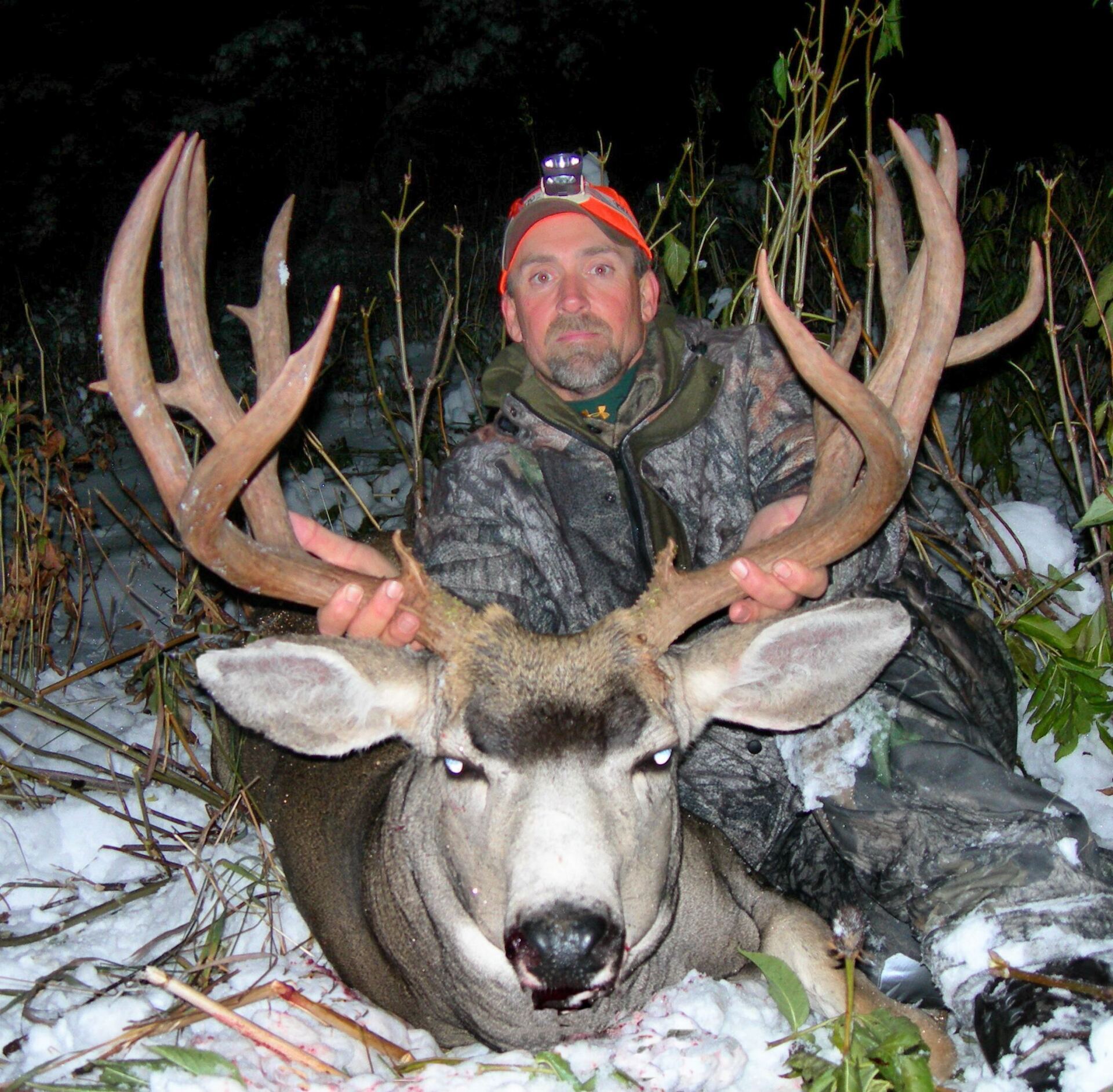 Hunter in camo holds large buck with impressive antlers in snowy setting.