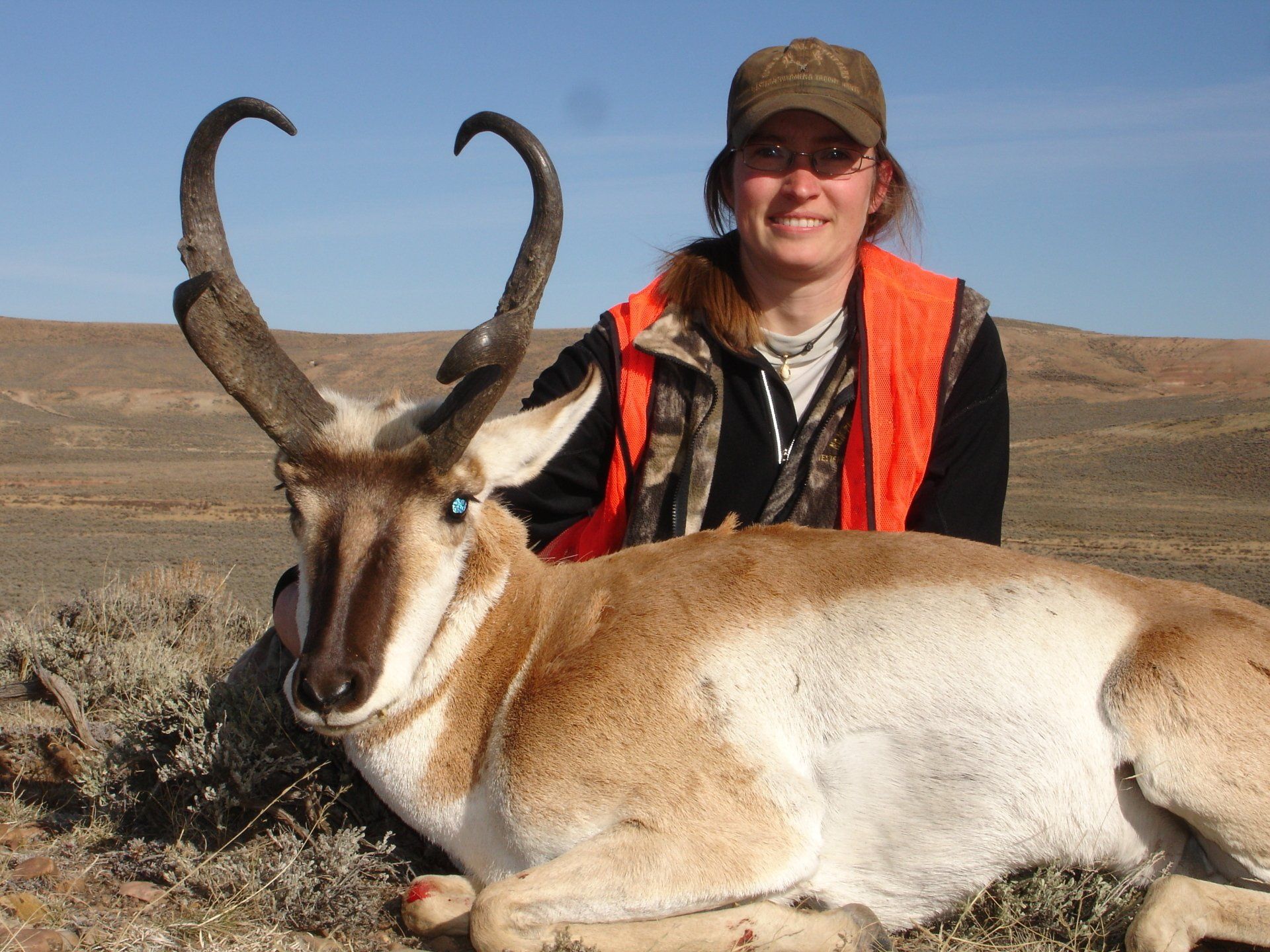 Woman in hunting gear smiles next to a pronghorn antelope in a Wyoming desert setting.