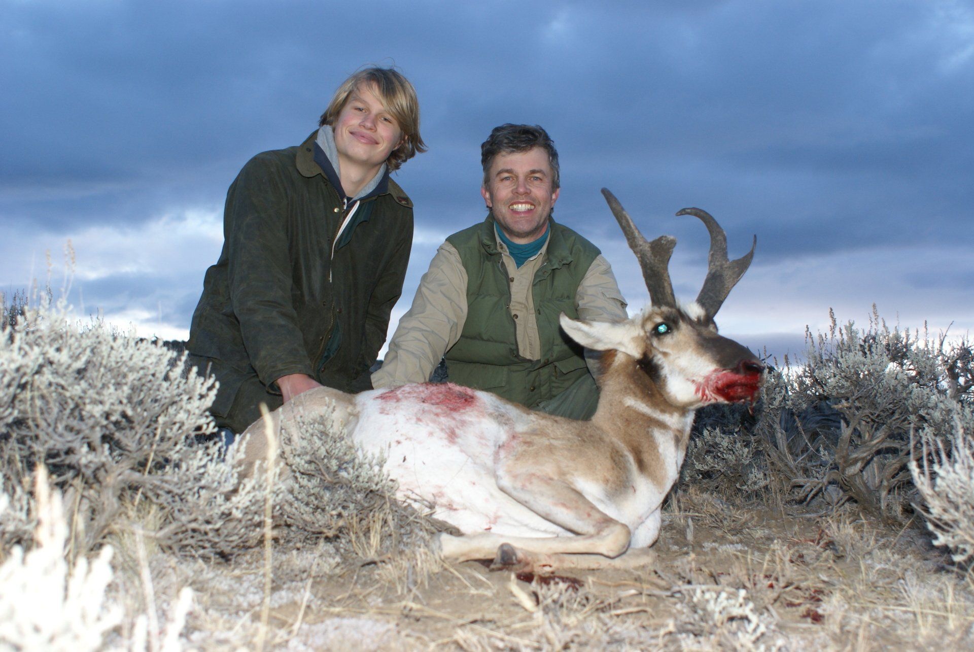 Two people pose with a Wyoming pronghorn antelope in a field. 