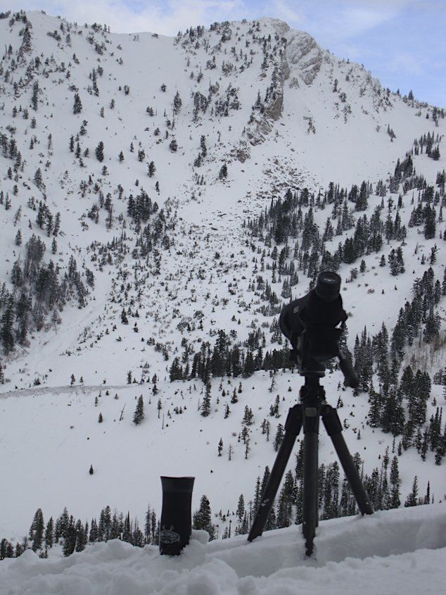 Snow-covered mountain scene. A tripod with a camera and lens stand in front of the snowy landscape with trees.