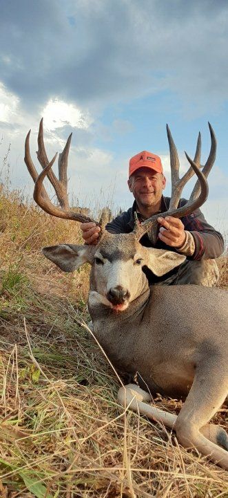 A person in an orange cap holds a large buck with impressive antlers, posing in a field.