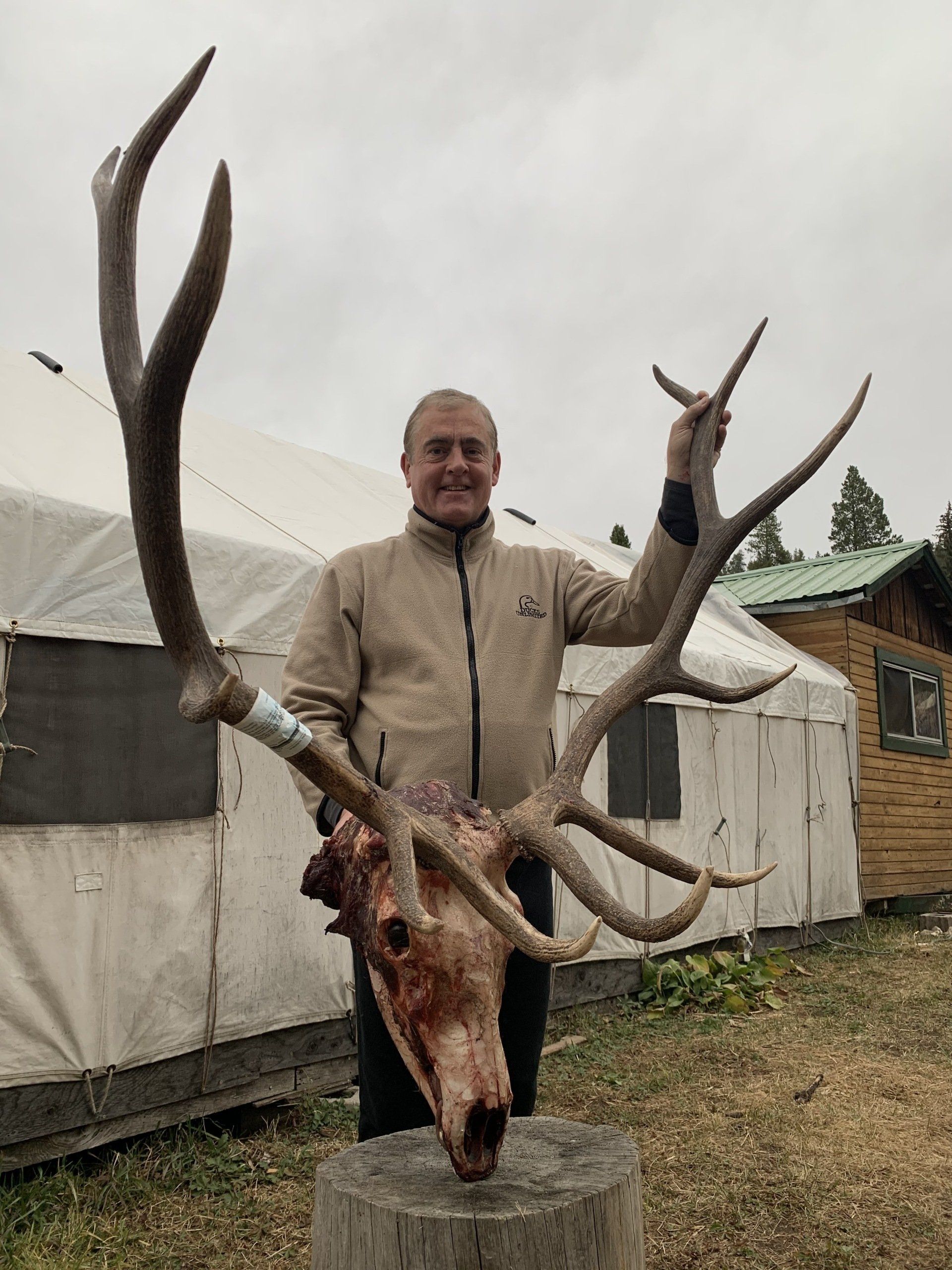 A man is holding a large deer skull in front of a tent