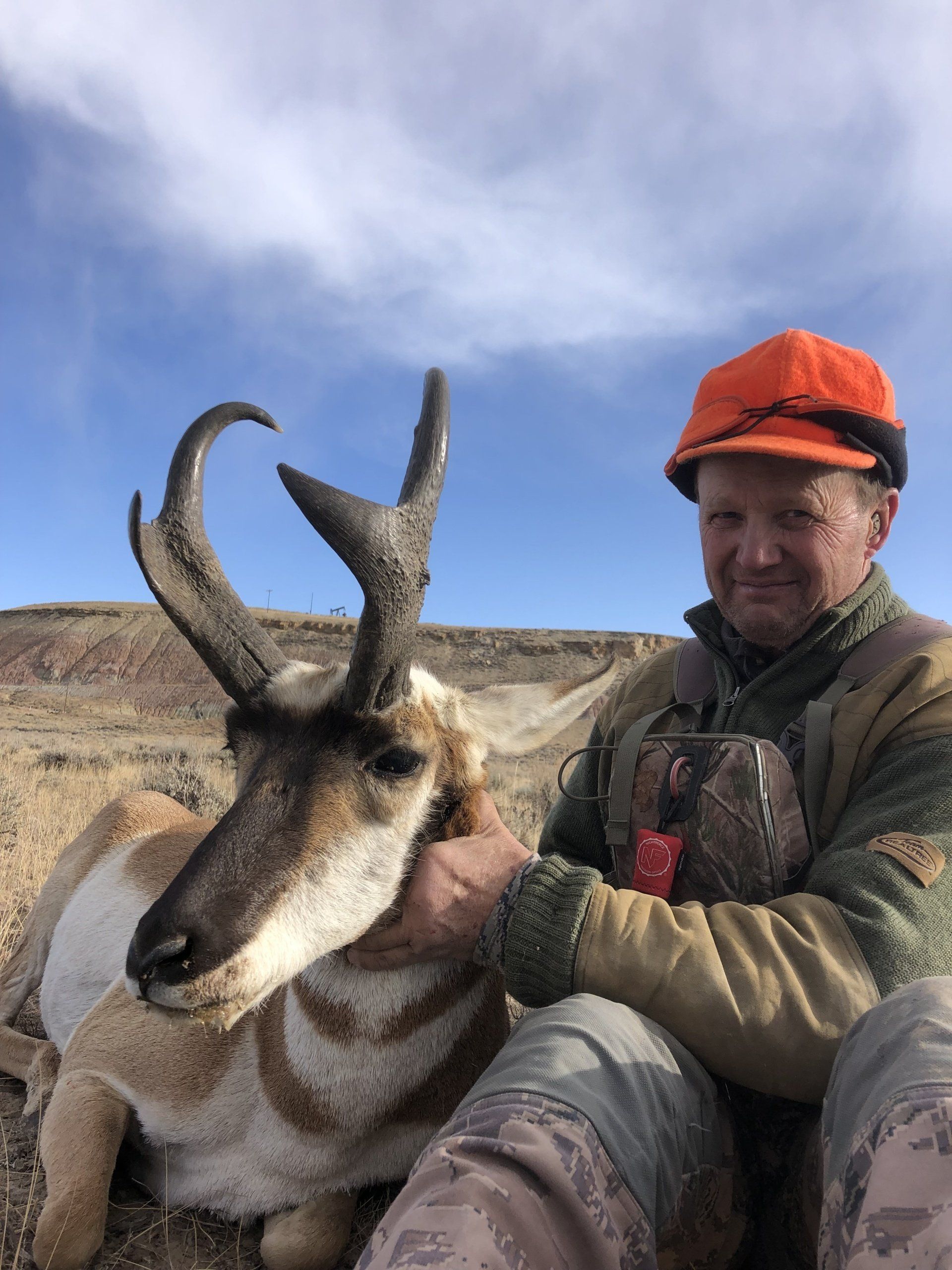 Hunter in orange hat with a trophy pronghorn antelope in a Wyoming desert landscape.