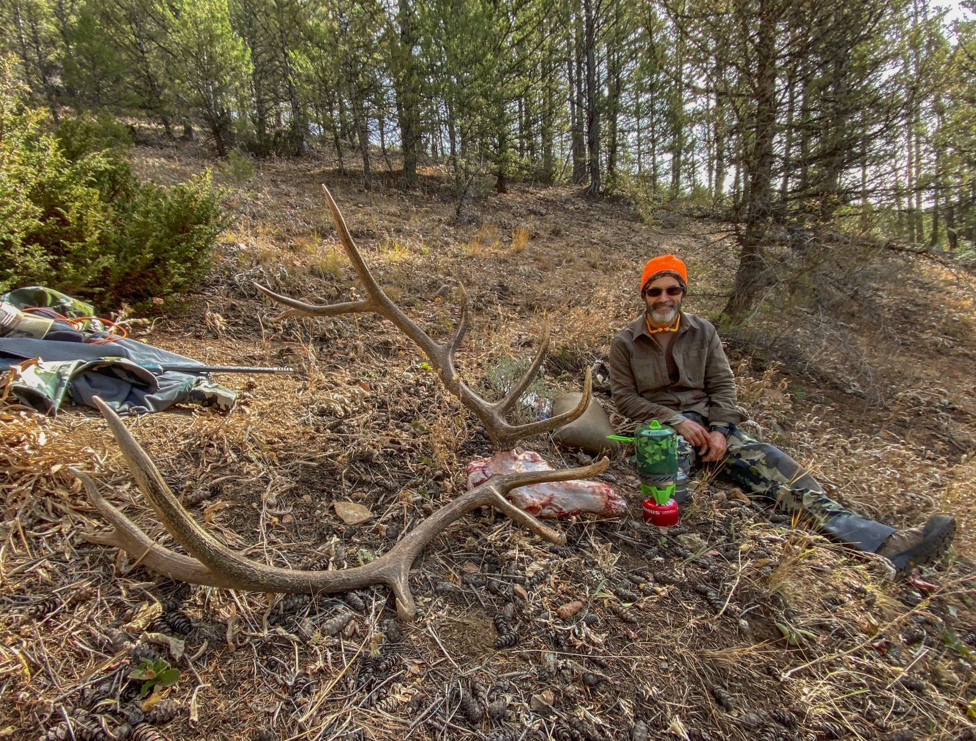 A man is sitting in the woods next to a deer skull