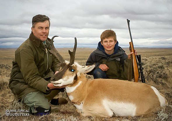 Man and boy with a pronghorn antelope in a field. Cloudy sky.