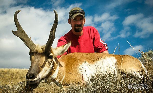 Man with a Wyoming pronghorn antelope in grassy field; sunny sky.