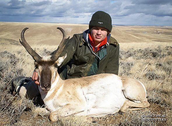 Hunter with a pronghorn in a grassy field; cloudy sky in the background.