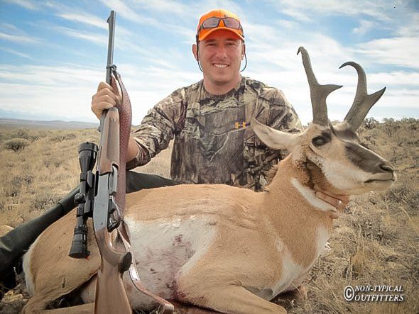 Hunter with a harvested pronghorn antelope, outdoors in a dry, grassy landscape.