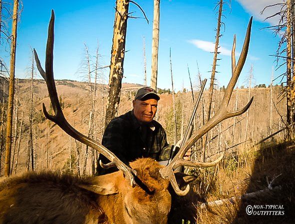 Hunter with large elk antlers in a forest setting.