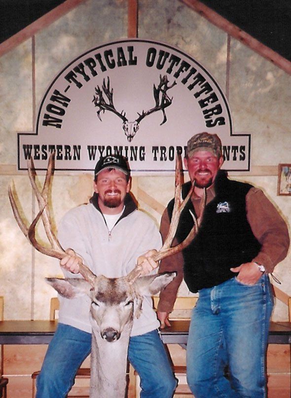 Two men pose with a deer trophy in front of 