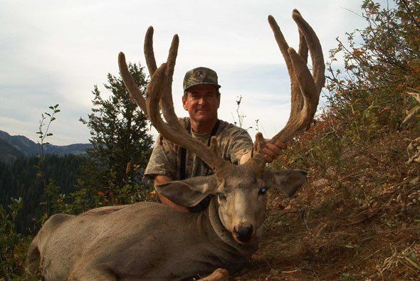 Man poses with large buck deer in outdoor setting.