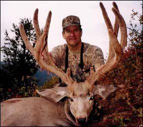 Hunter in camouflage with a large-antlered deer. Outdoors, blurred background, sunny.