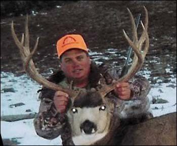 Man in orange hat holds large deer antlers; snowy outdoor setting.