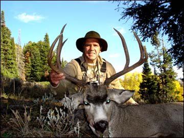 Hunter in hat with large deer antlers, smiling, outdoors.