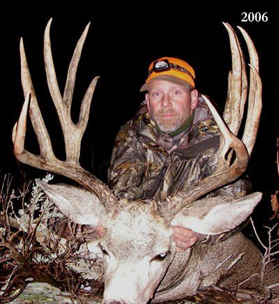 Man in camo holds large buck with impressive antlers at night.