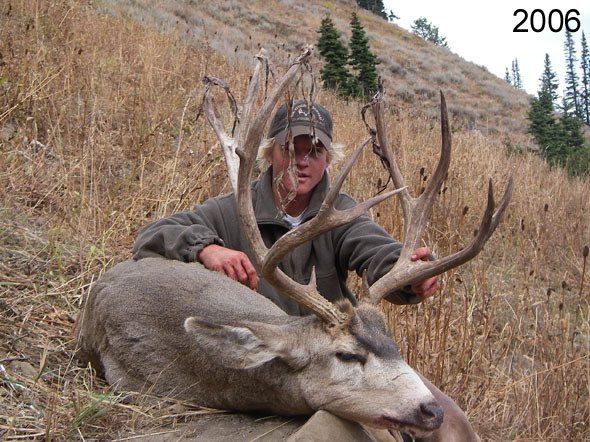 Man in cap with a large buck deer, antlers prominent, in a field, dated 2006.