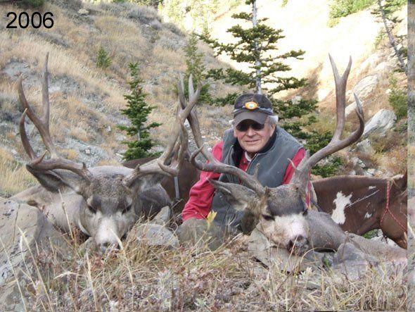 Man poses with two harvested deer in mountainous terrain.