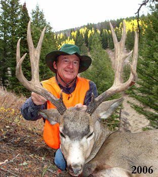 Man in orange vest holding a large buck with impressive antlers in a forest setting.