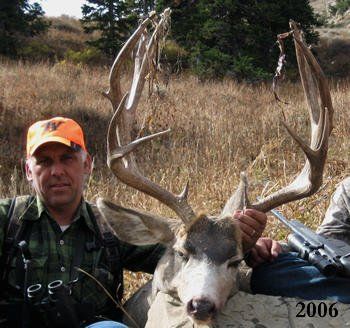 Hunter holding large antlered deer in a grassy field, wearing orange hat.
