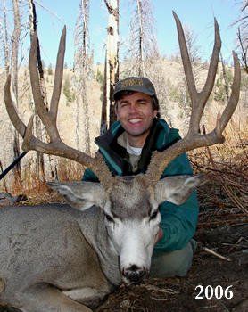 Man kneels beside a large buck with impressive antlers, smiling outdoors, dated 2006.