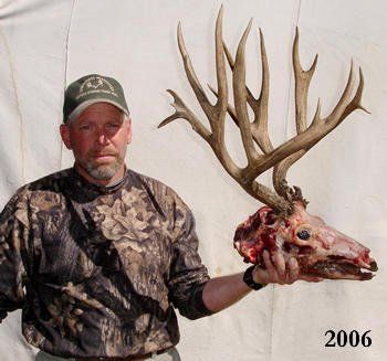 Man in camouflage holding elk skull with large antlers, dated 2006.