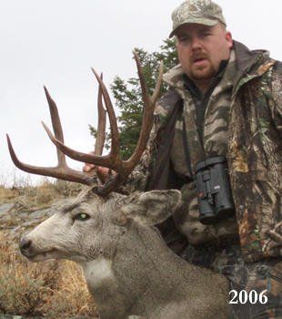 Man in camo with a large-antlered deer. Outdoors, holding antlers. 2006.