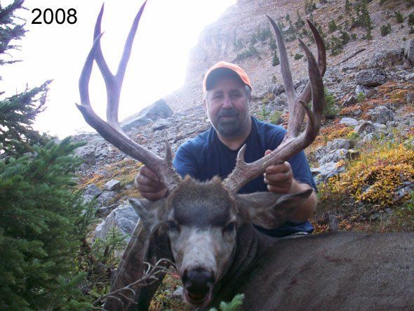 Man holding large antlered deer, mountain setting.