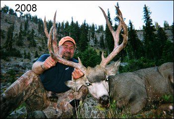 Man kneeling with large antlered deer; mountains in background, 2008.