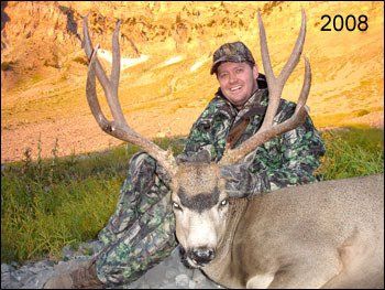 Hunter in camouflage next to large deer with impressive antlers, 2008 in background.