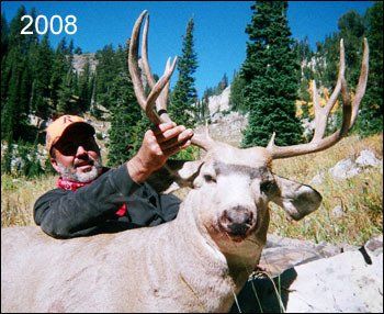 Man holding a large mule deer with impressive antlers in a mountain setting.