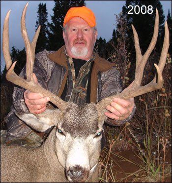 Man in orange hat holds large deer antlers, 2008. Setting: outdoor, trees visible.