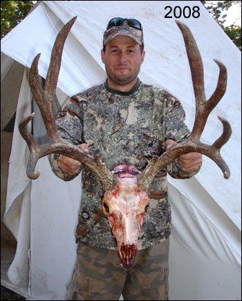 Man holding deer skull with large antlers; camouflage clothing, tent background, 