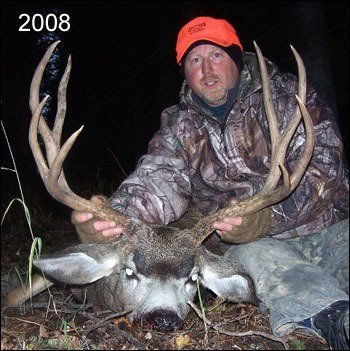 Hunter in camouflage holds a large buck with impressive antlers, orange cap, night setting, 2008.