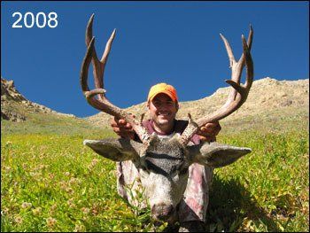 Man in orange hat holding deer antlers in a green field, sunny blue sky, 2008.
