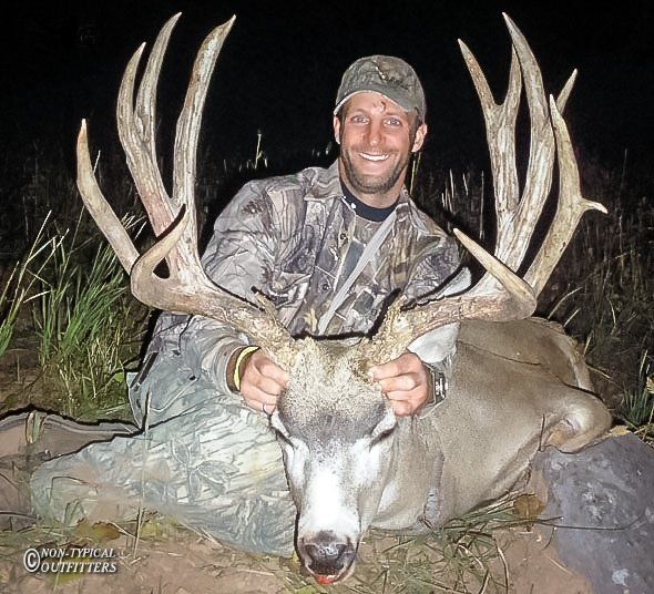 A man in a camo jacket is holding a large deer