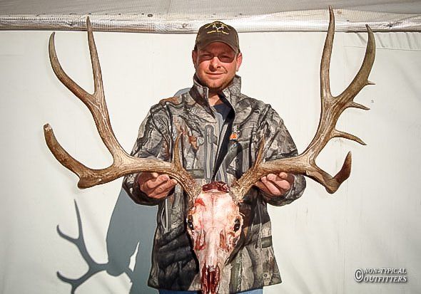 A man in a camo jacket is holding a deer skull