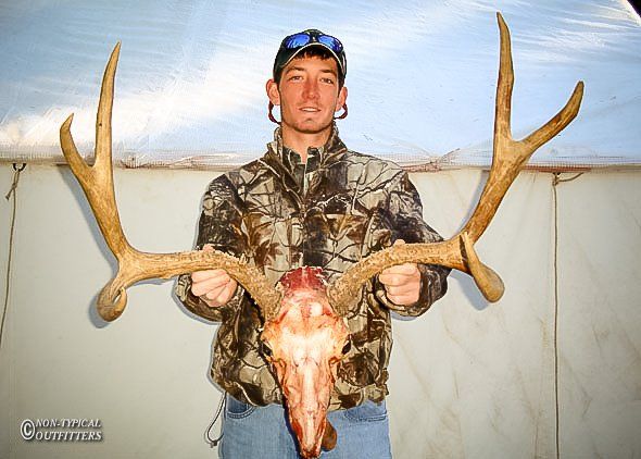 A man in a camo jacket is holding a deer skull