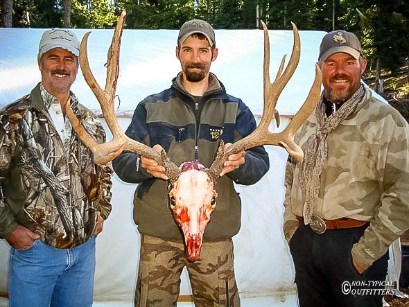 Three men standing next to each other holding a deer skull