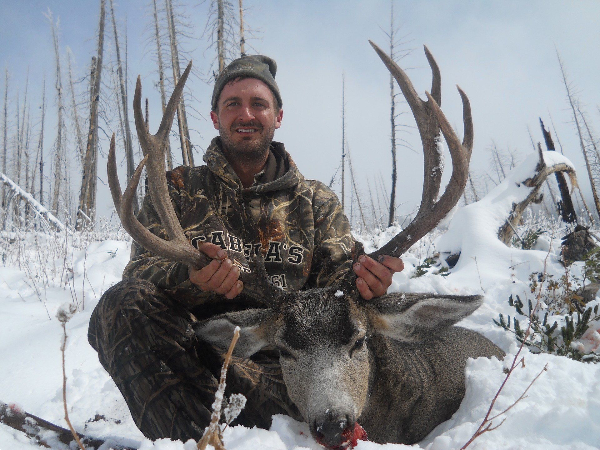 A man in a camo jacket holds a deer in the snow