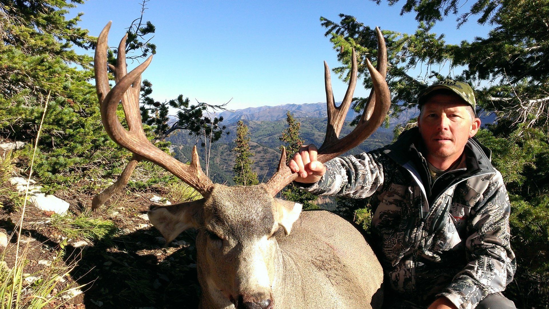 A man in a camo jacket is holding a large deer