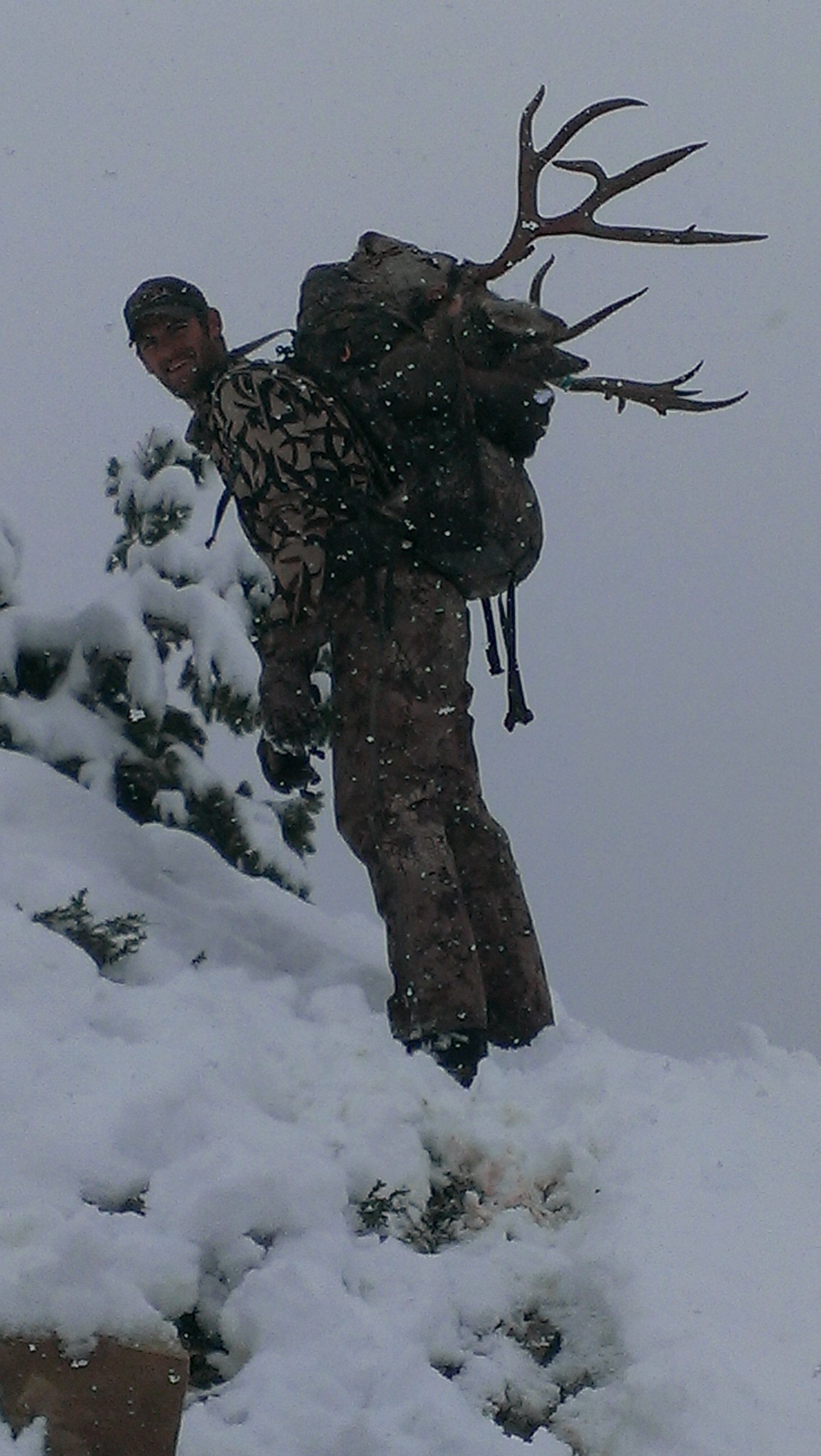 A man is standing in the snow with a deer antlers on his back