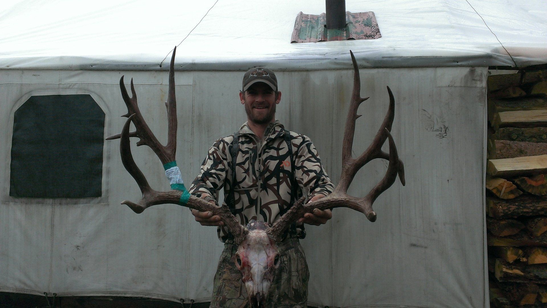A man standing in front of a tent holding a large deer